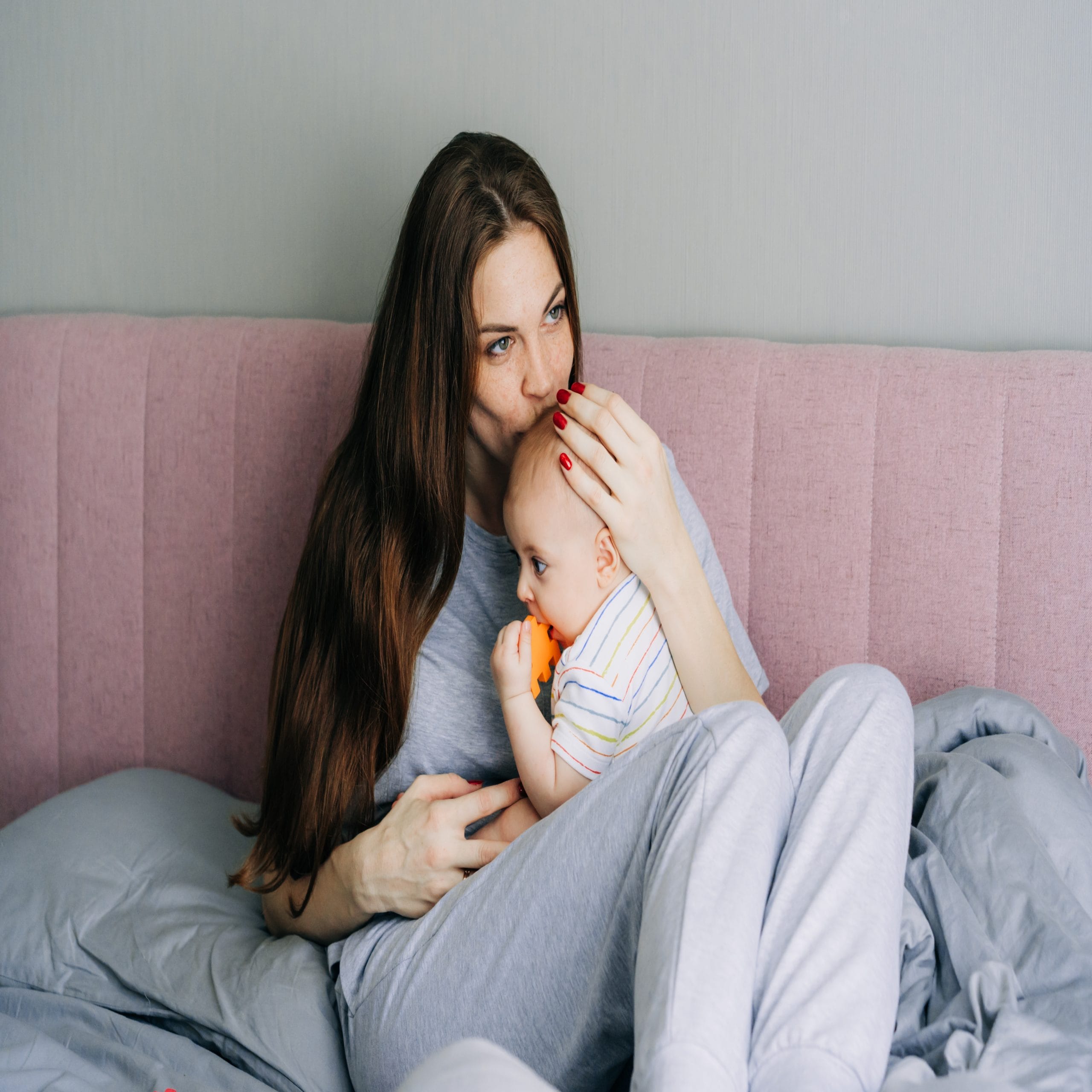 postpartum hair loss: mother with long hair sits on bed with baby