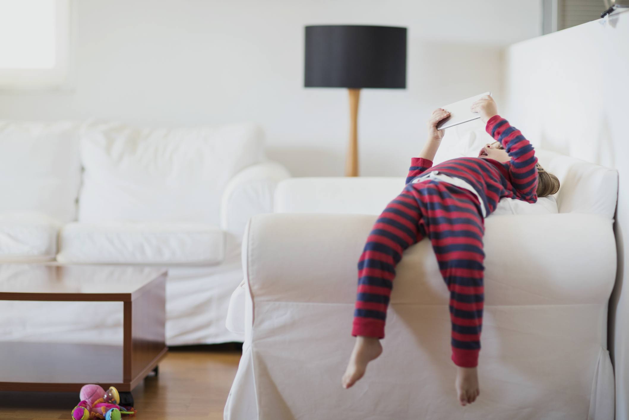 2 year old boy lying on a bed using a tablet, wondering how screen time affects babies