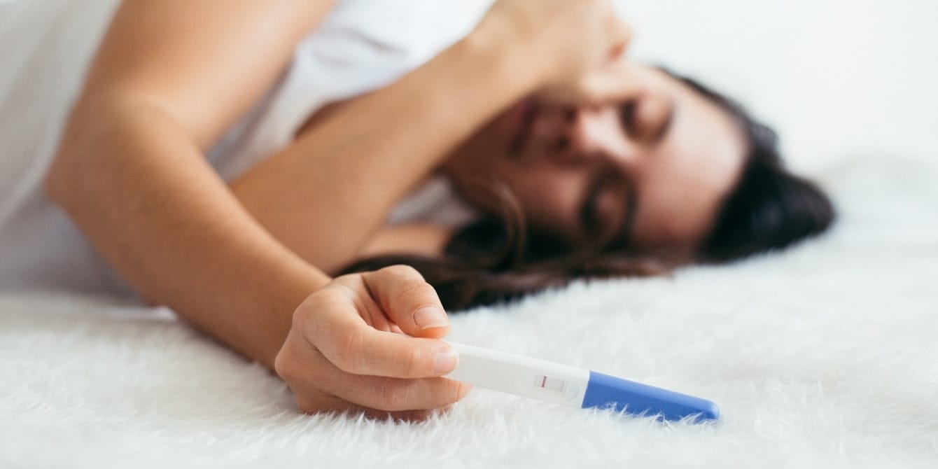 sad woman laying down with negative pregnancy test - pregnant