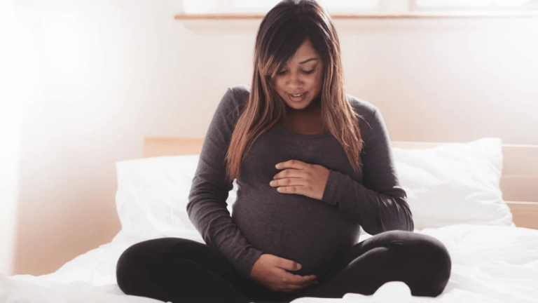 woman holding pregnant belly as she sits on bed