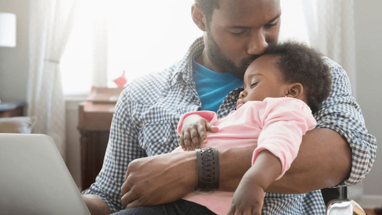 dad working on a laptop and kissing daughter on the head