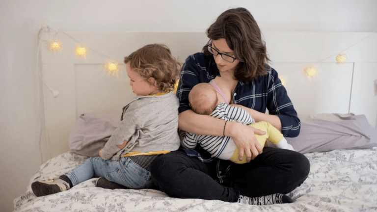 mom breastfeeding newborn while child sits beside