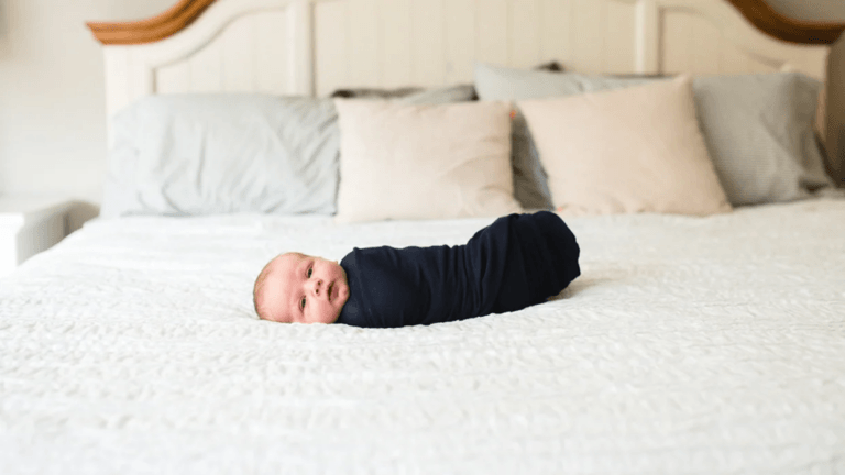 swaddled baby laying on a bed, one of motherly's favorite baby picture ideas