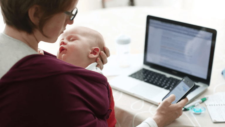 mom carrying baby while on her phone and laptop