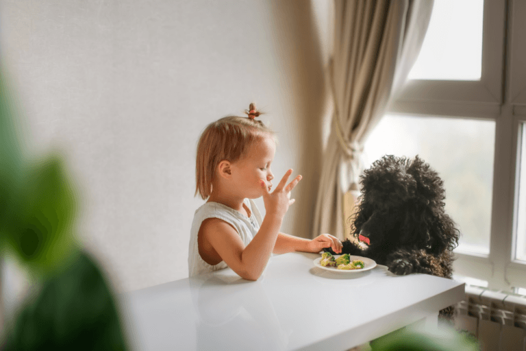 child eating veggies with dog watching