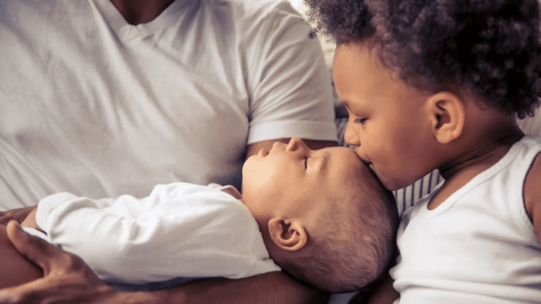 older child kissing newborn on the head