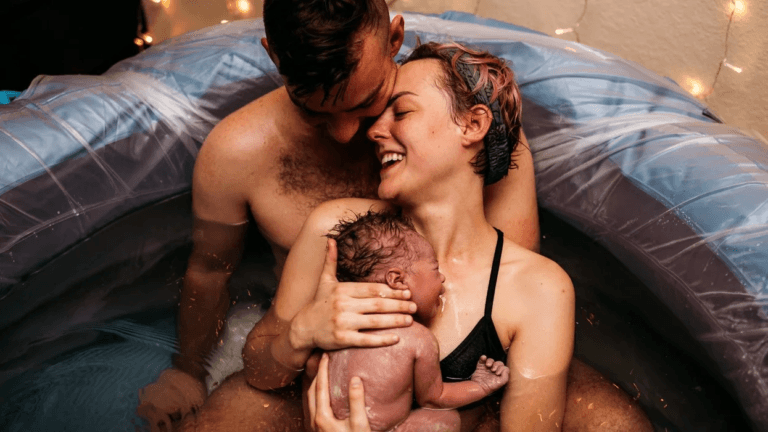 partner behind woman holding a baby just after a home birth