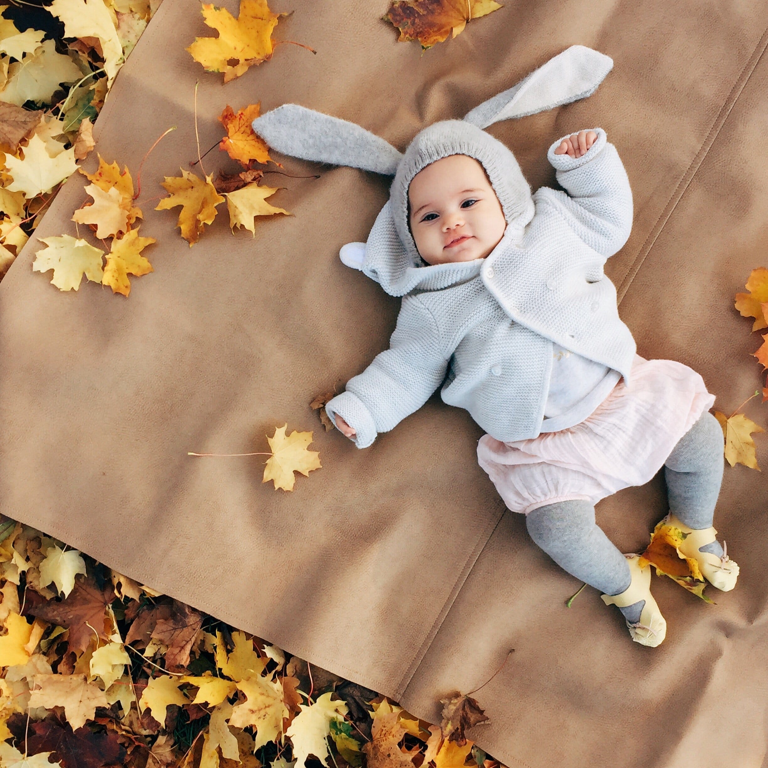 baby with bunny sweater lying next to leaves- november babies