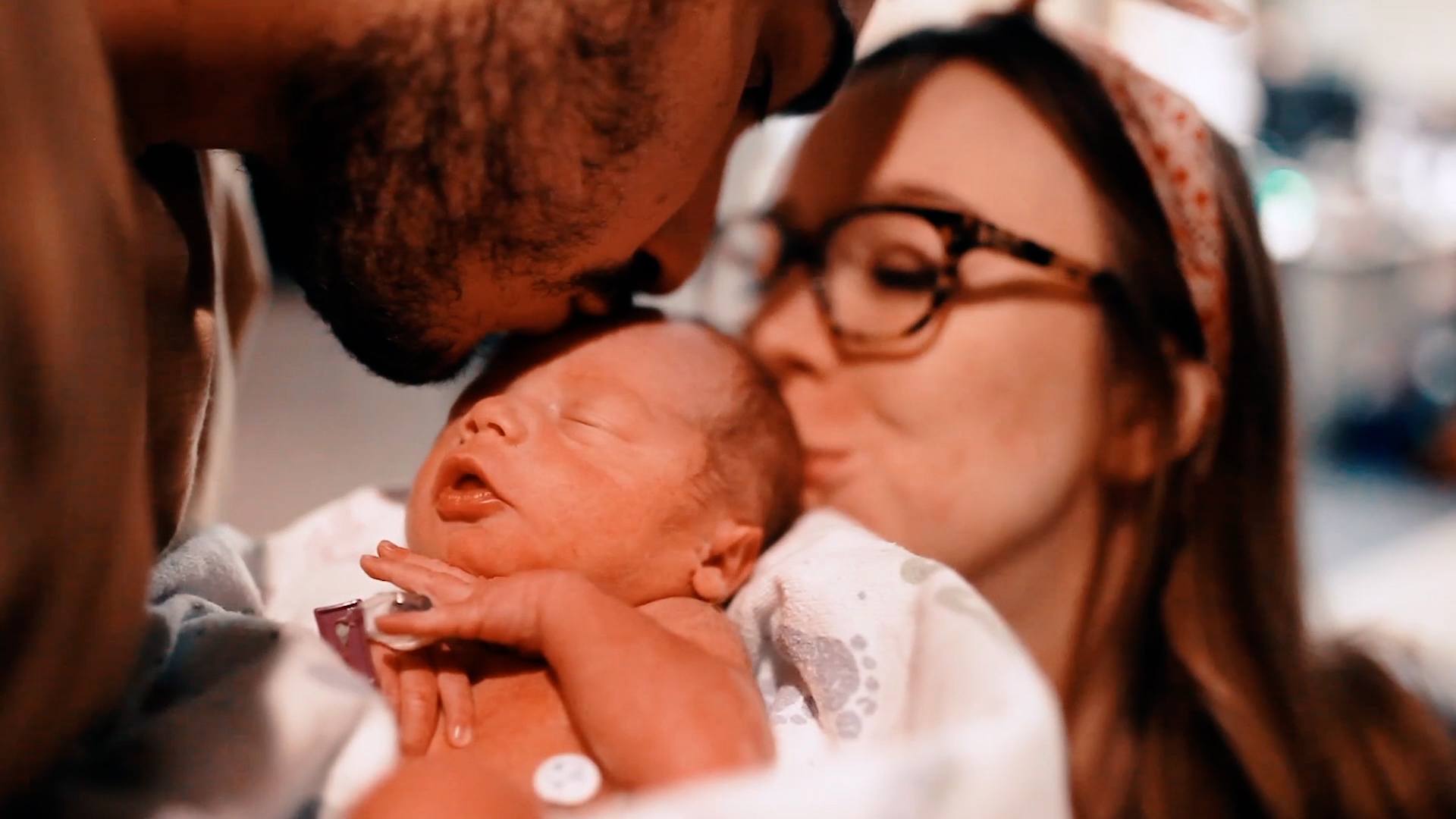 parents kissing newborn baby on the forehead