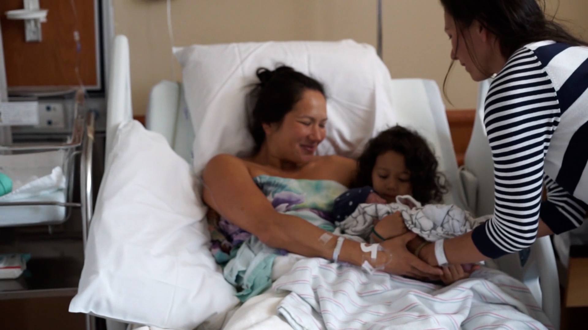 woman holding newborn baby with sister beside her