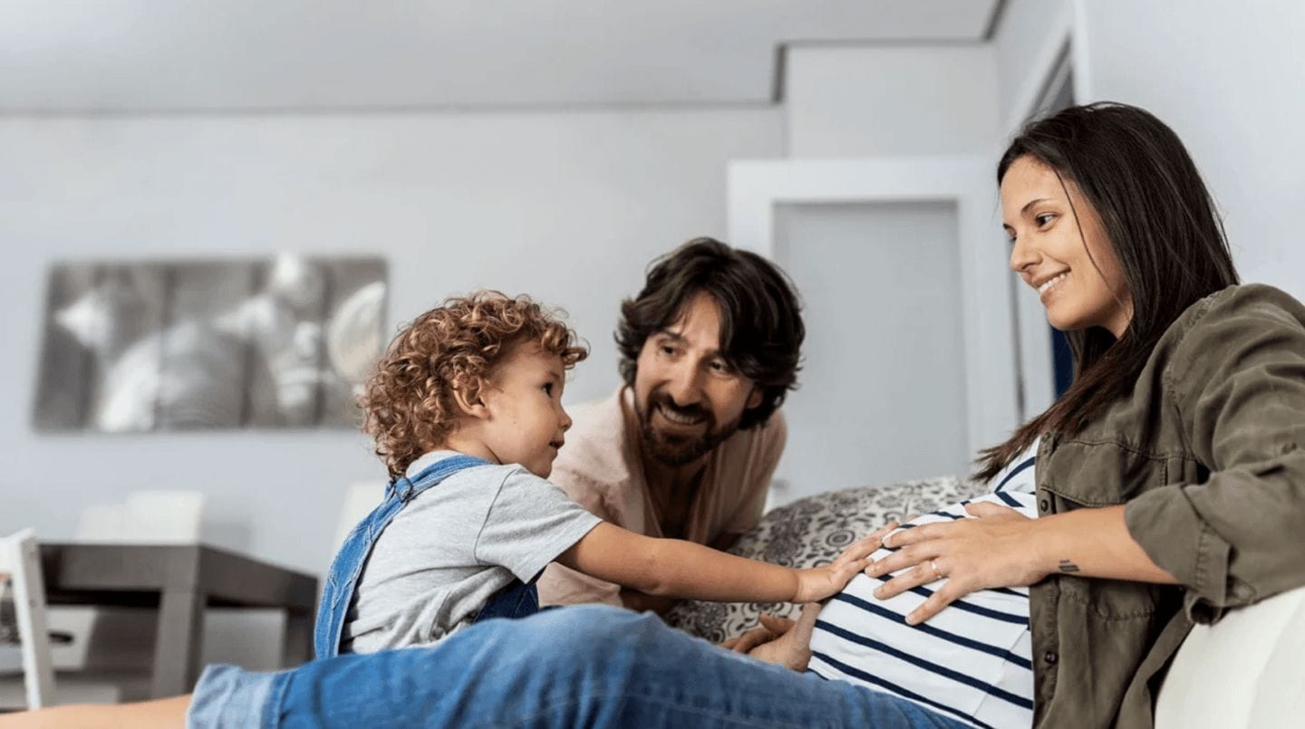 toddler touching pregnant moms belly while dad watches - do second babies come earlier