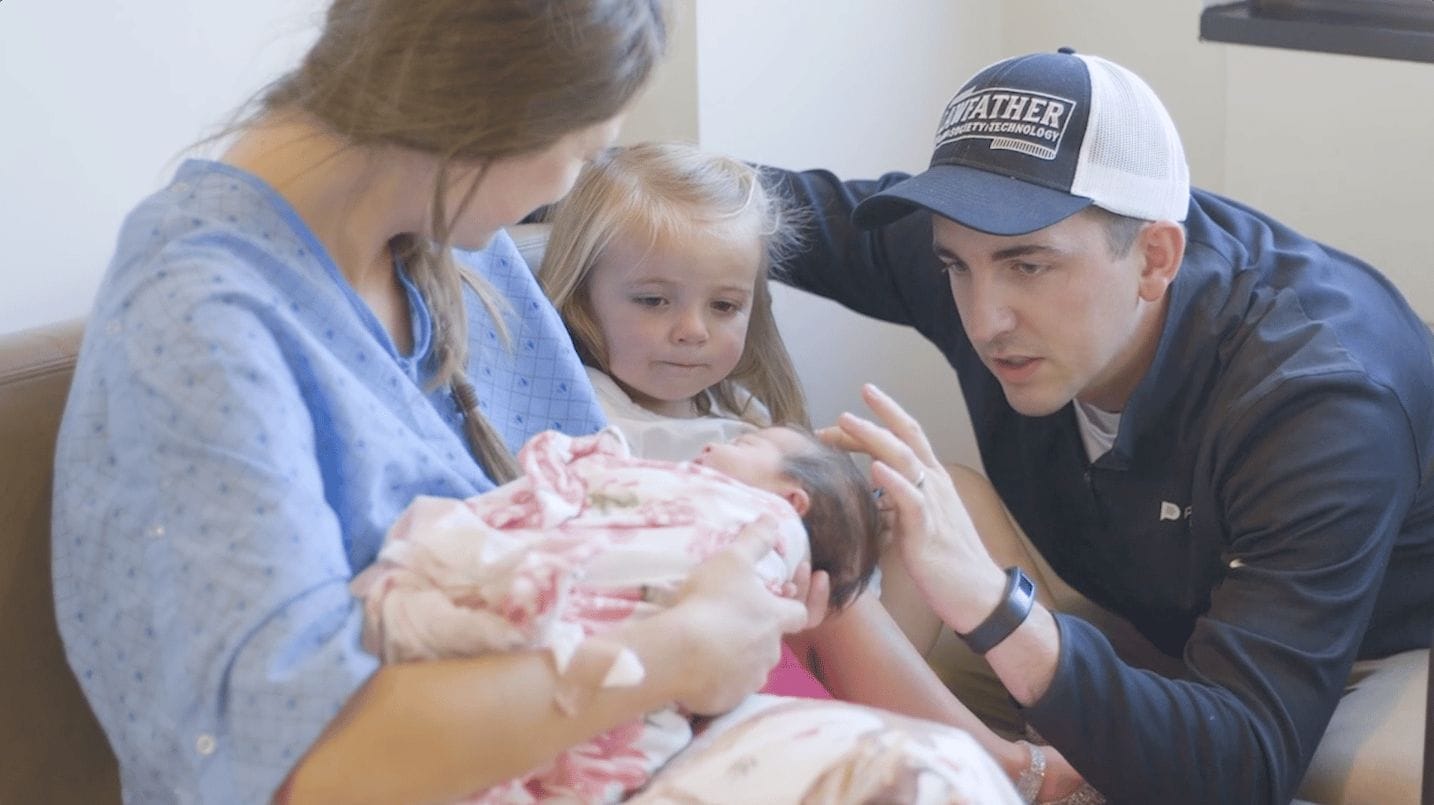 mom holding a newborn baby while dad and toddler look