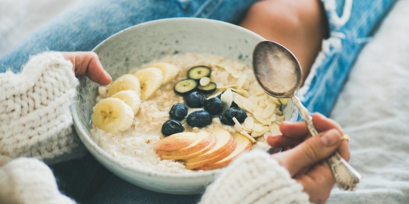 woman holding bowl of oatmeal with spoon - foods that boost your milk supply