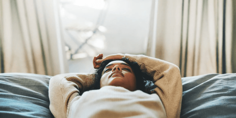 woman laying down with her hands above her head in an act of self care for moms