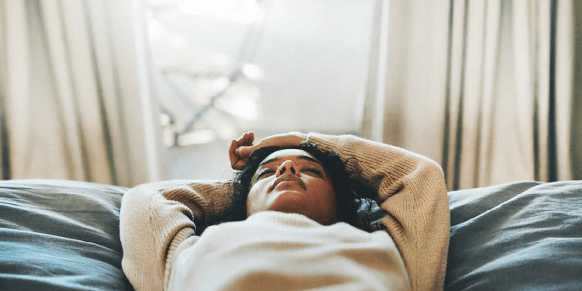 woman laying down with her hands above her head in an act of self care for moms