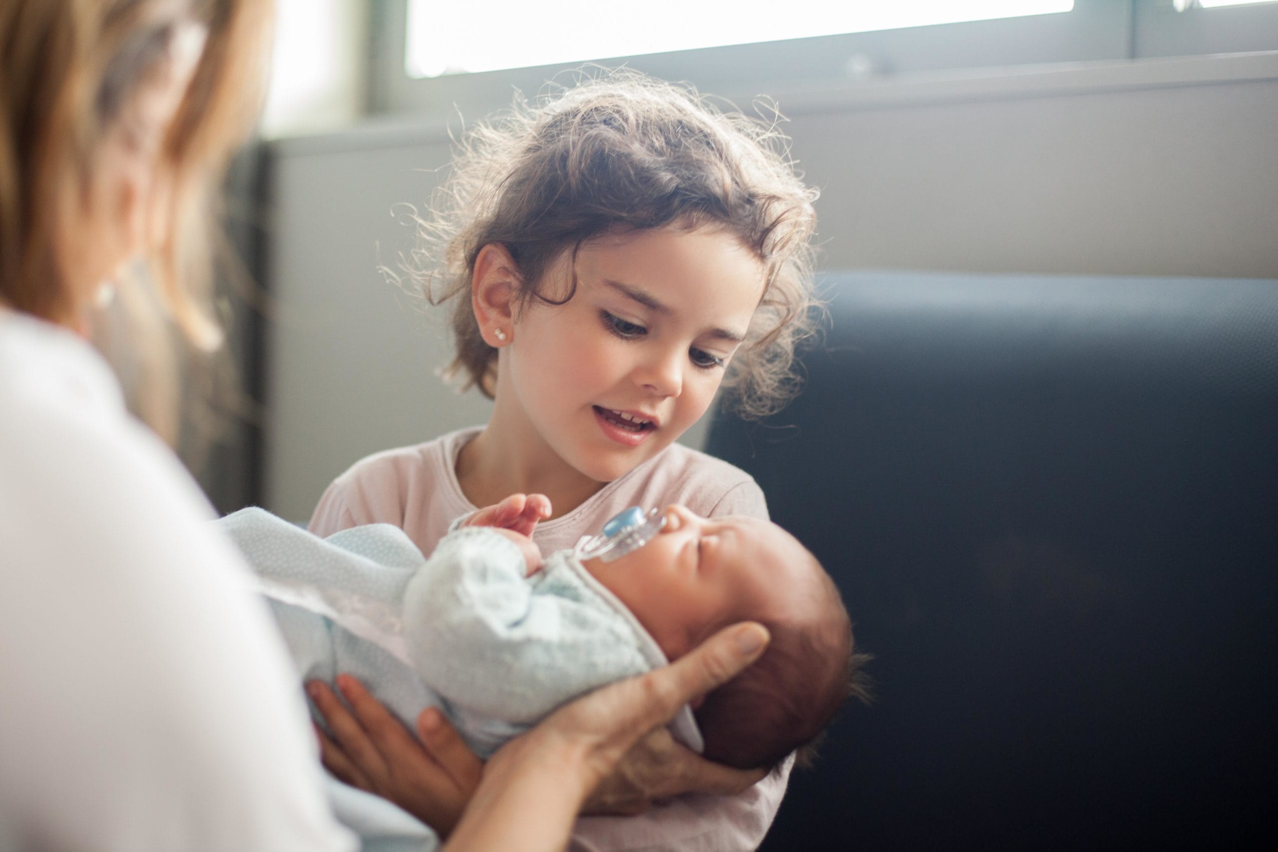 mom helping older sibling hold baby after giving birth the second time