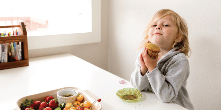 little girl holding a muffin in front of breakfast food on a table - words that transformed a picky eater