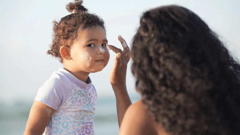 mom putting sunscreen on a toddler at a beach