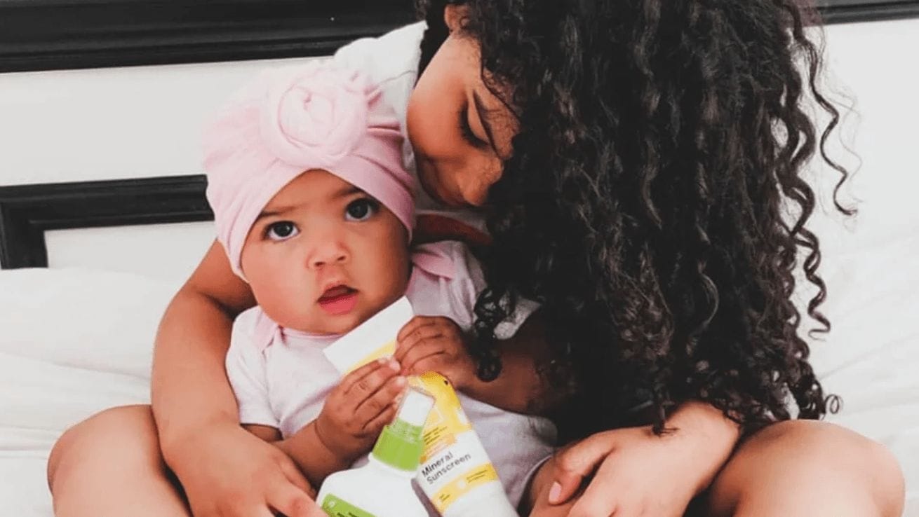 mom snuggling baby holding sunscreen