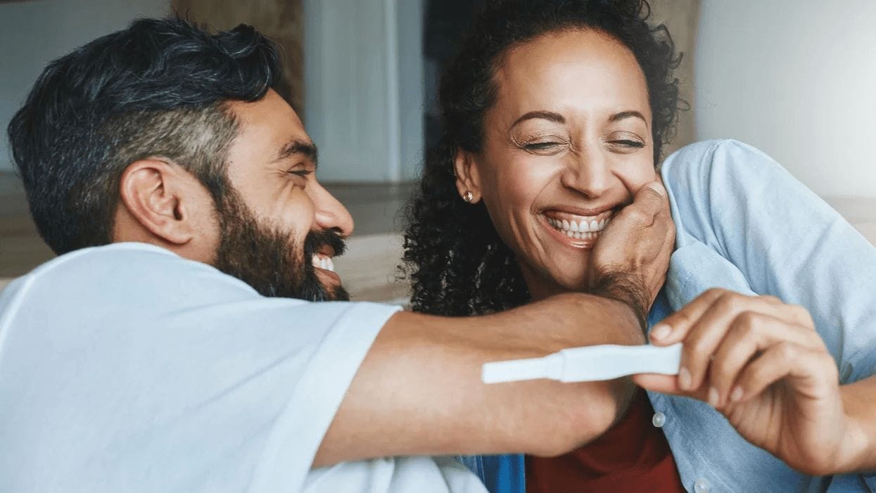 partners embracing with a pregnancy test in hand after noticing early signs of pregnancy