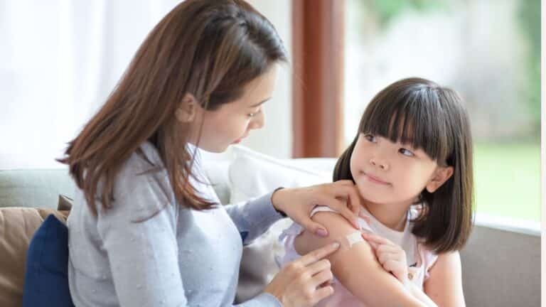 mom helping little girl with a bandaid - flu shot before Halloween