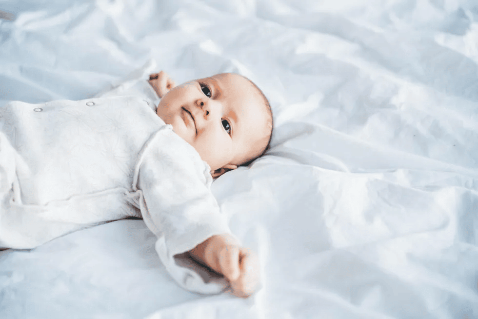 baby wearing a sleep sack laying on a bed - 5-week-old baby feeding schedule