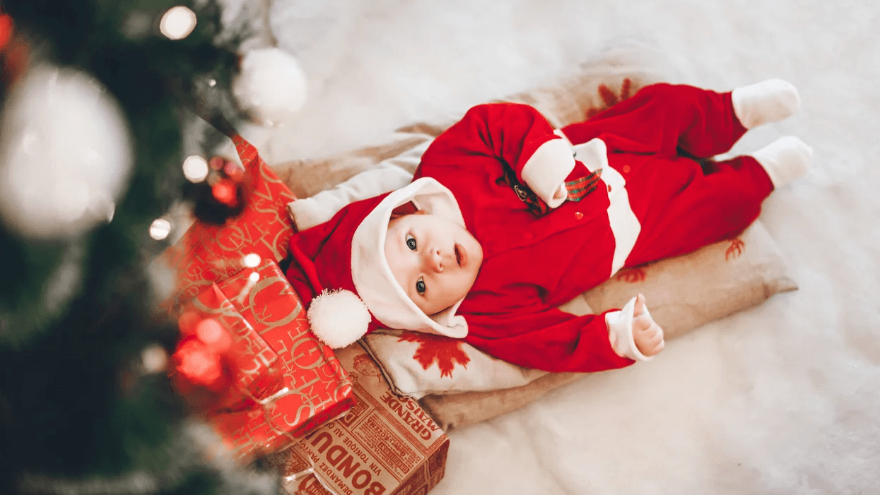 baby wearing santa pajamas laying under a christmas tree- baby's first christmas