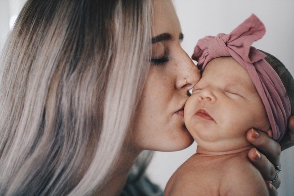 mother kissing newborn baby on the cheek