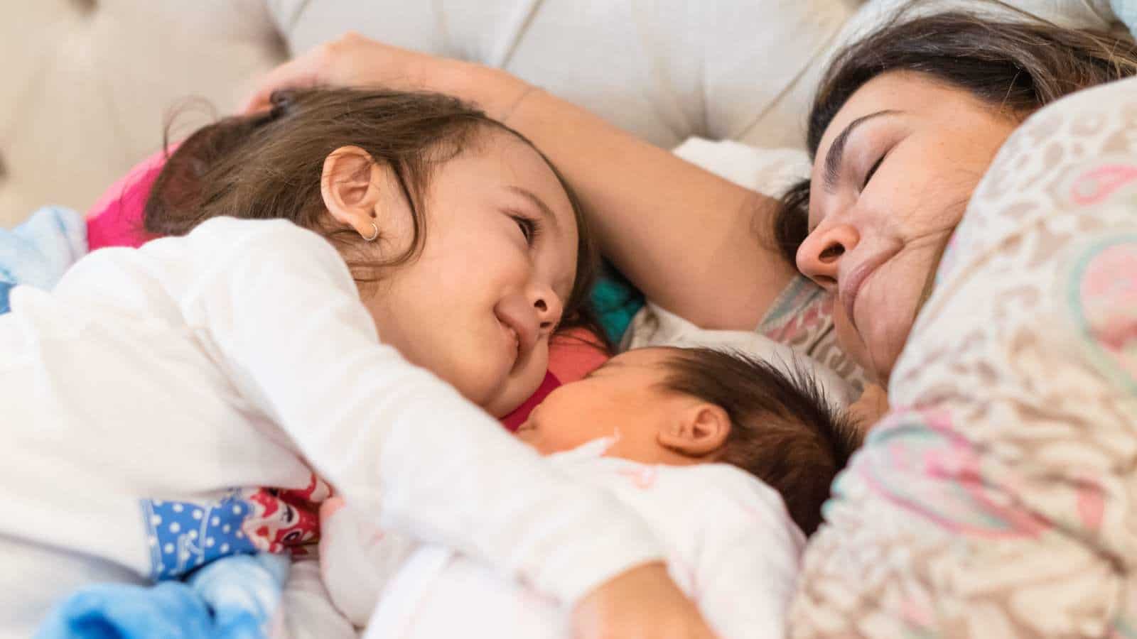 mom laying with toddler and newborn baby