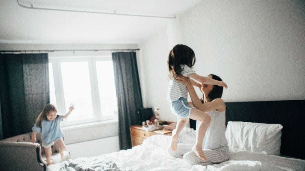 mom playing with two toddlers jumping on a bed