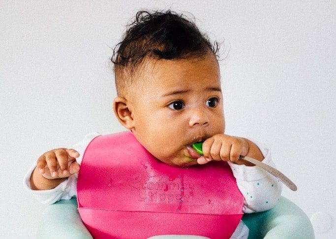 baby feeding itself a spoon with a silicone bib