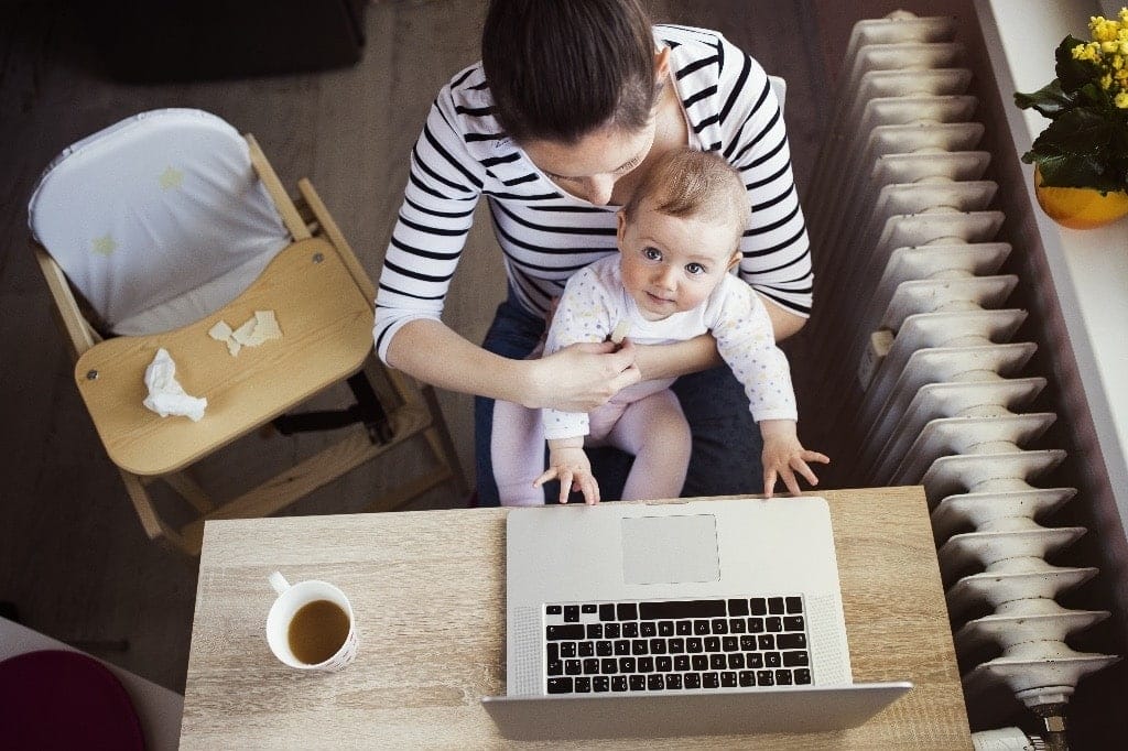 a woman holding a baby and looking at a laptop