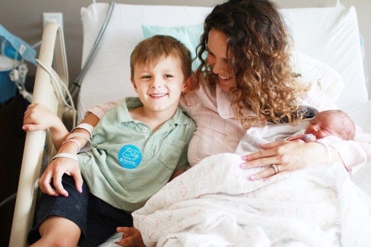 woman sitting in hospital bed with newborn and child