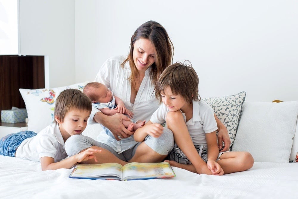 mom holding a newborn beside two siblings