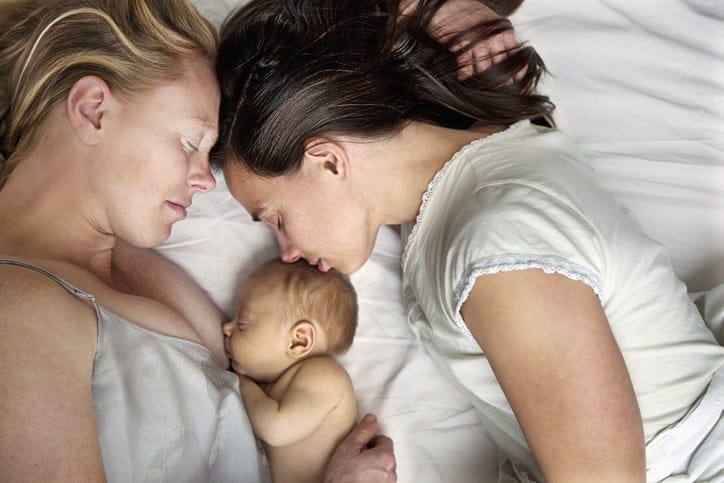 two moms laying on a bed with their baby between them