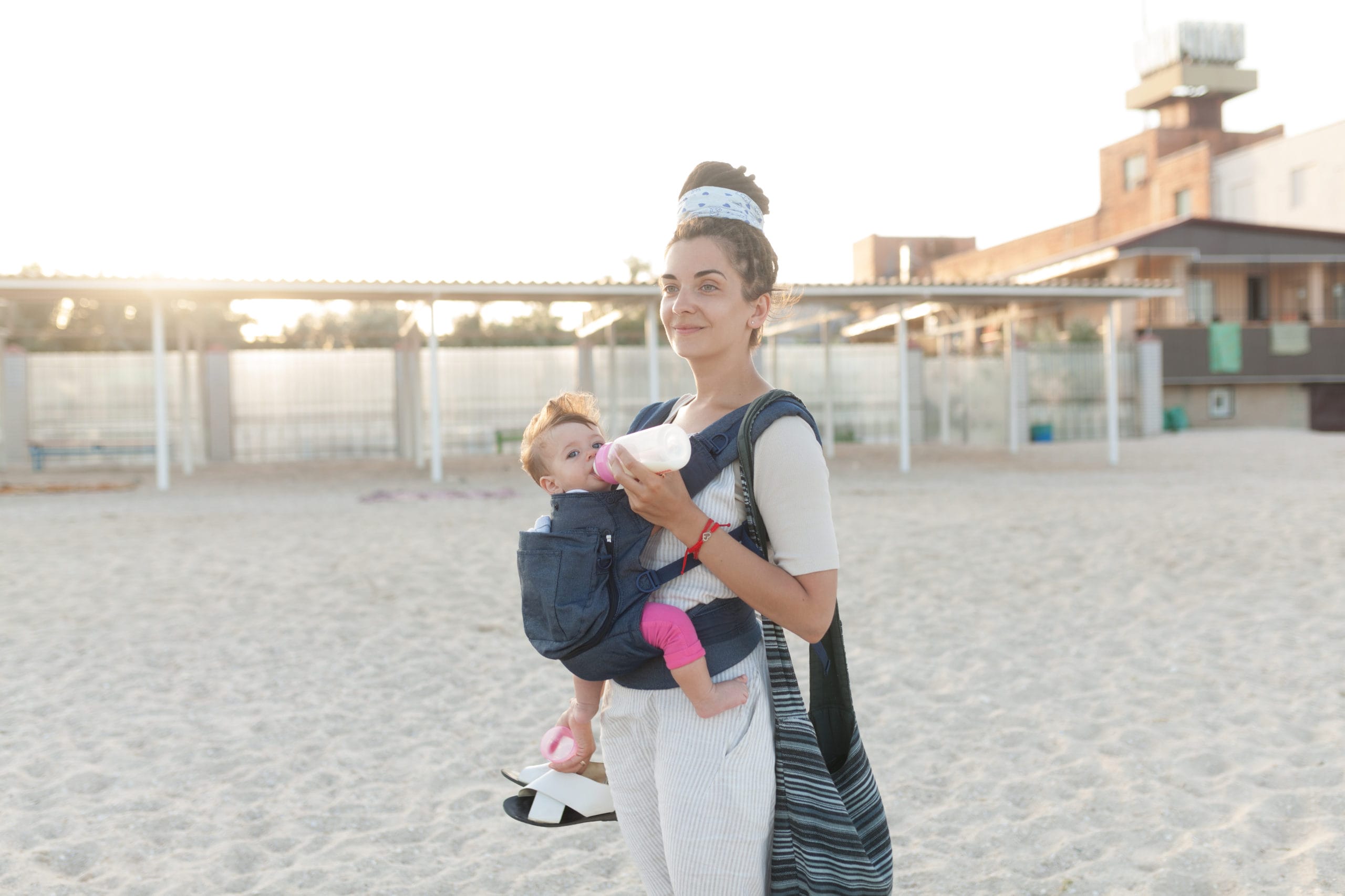 mom holding baby in a carrier on the beach