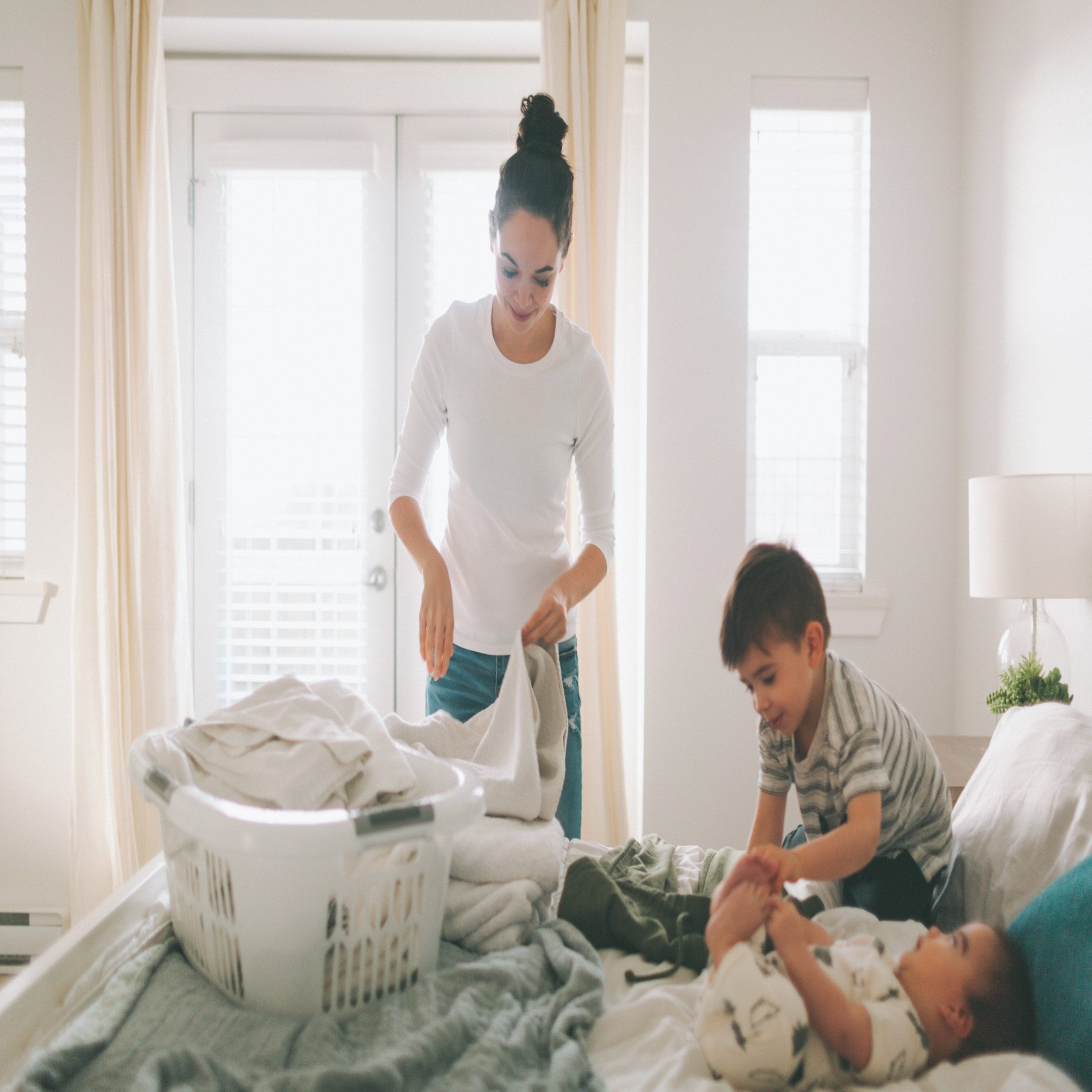 mom folding laundry while kid plays on bed