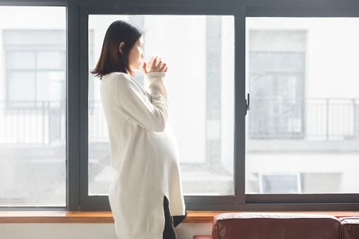 pregnant woman drinking water and looking outside a window