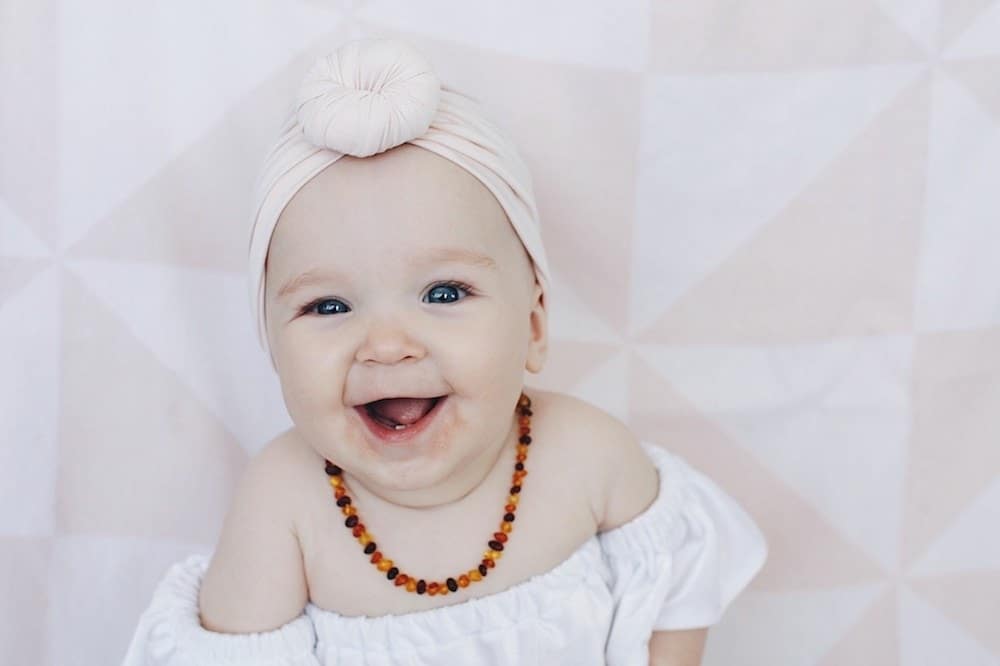 smiling baby wearing a headband and necklace- march babies