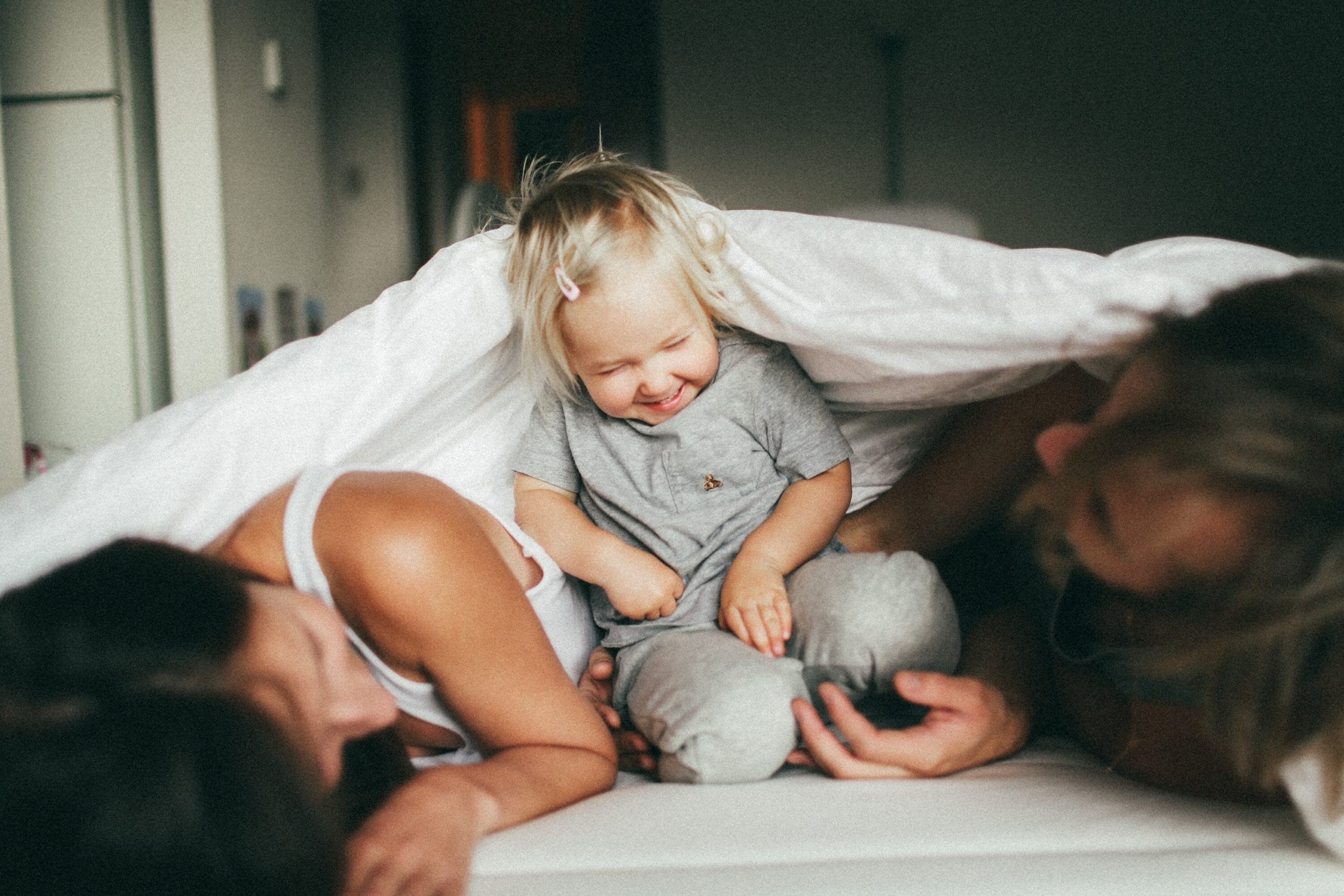 mom, dad and toddler playing on a bed