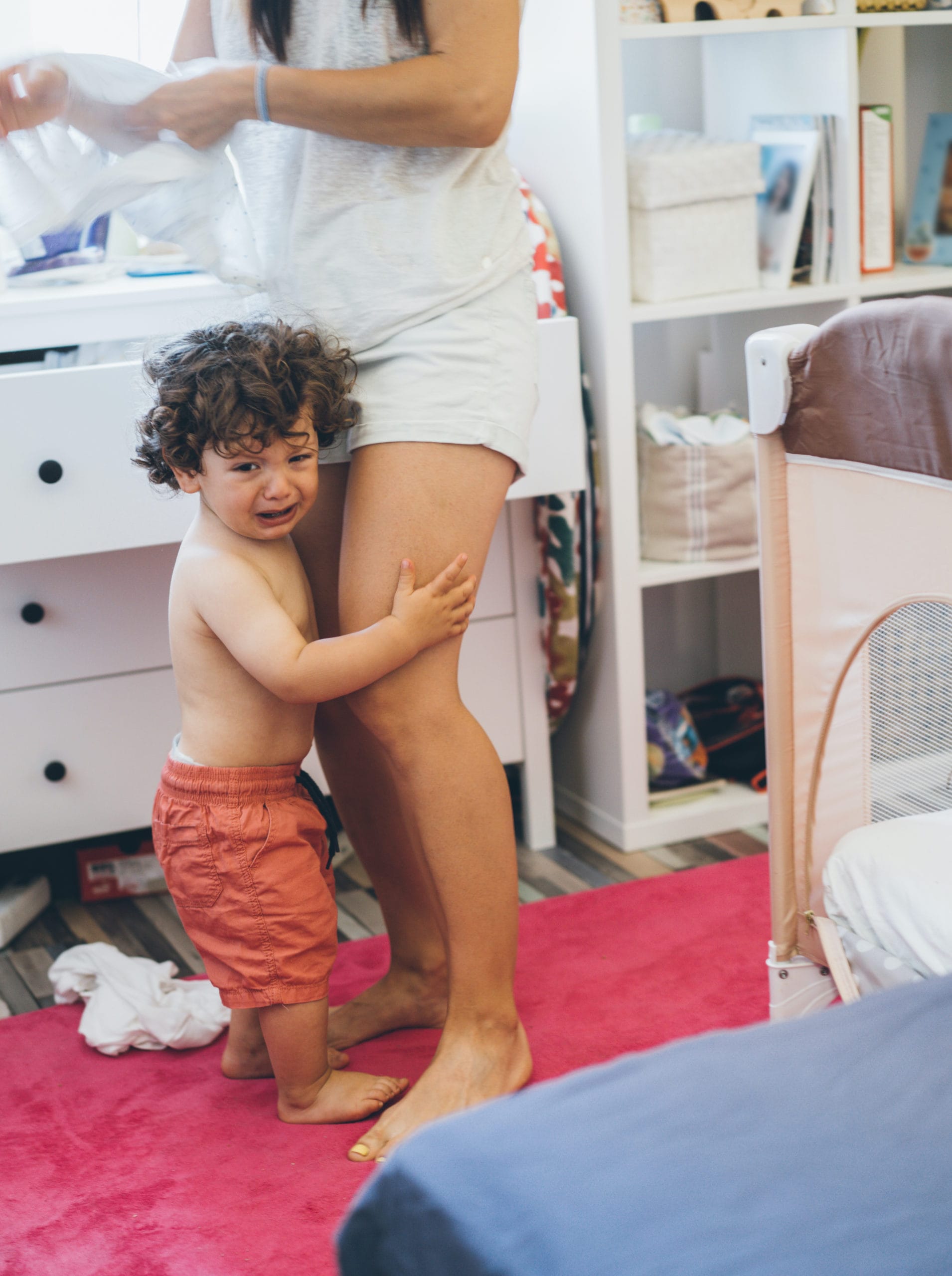 crying toddler hugging moms legs