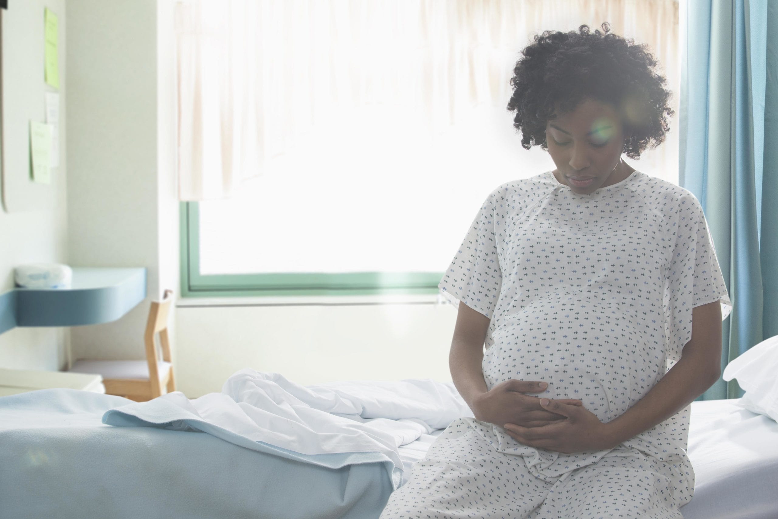 pregnant black woman sitting on the edge of a hospital bed