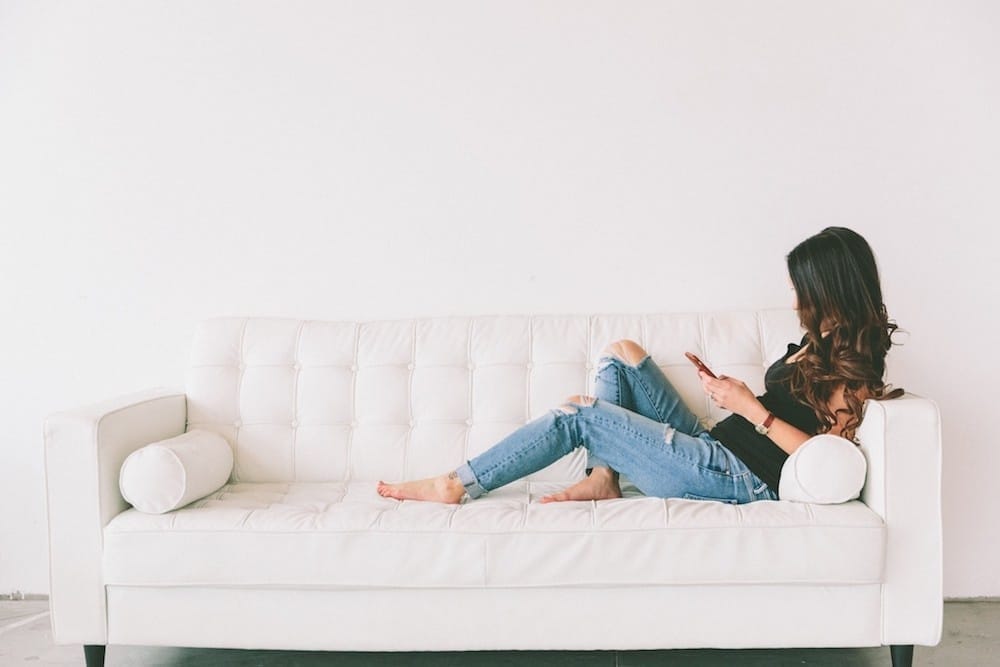 woman sitting on the couch on her phone - sleep when the baby sleeps