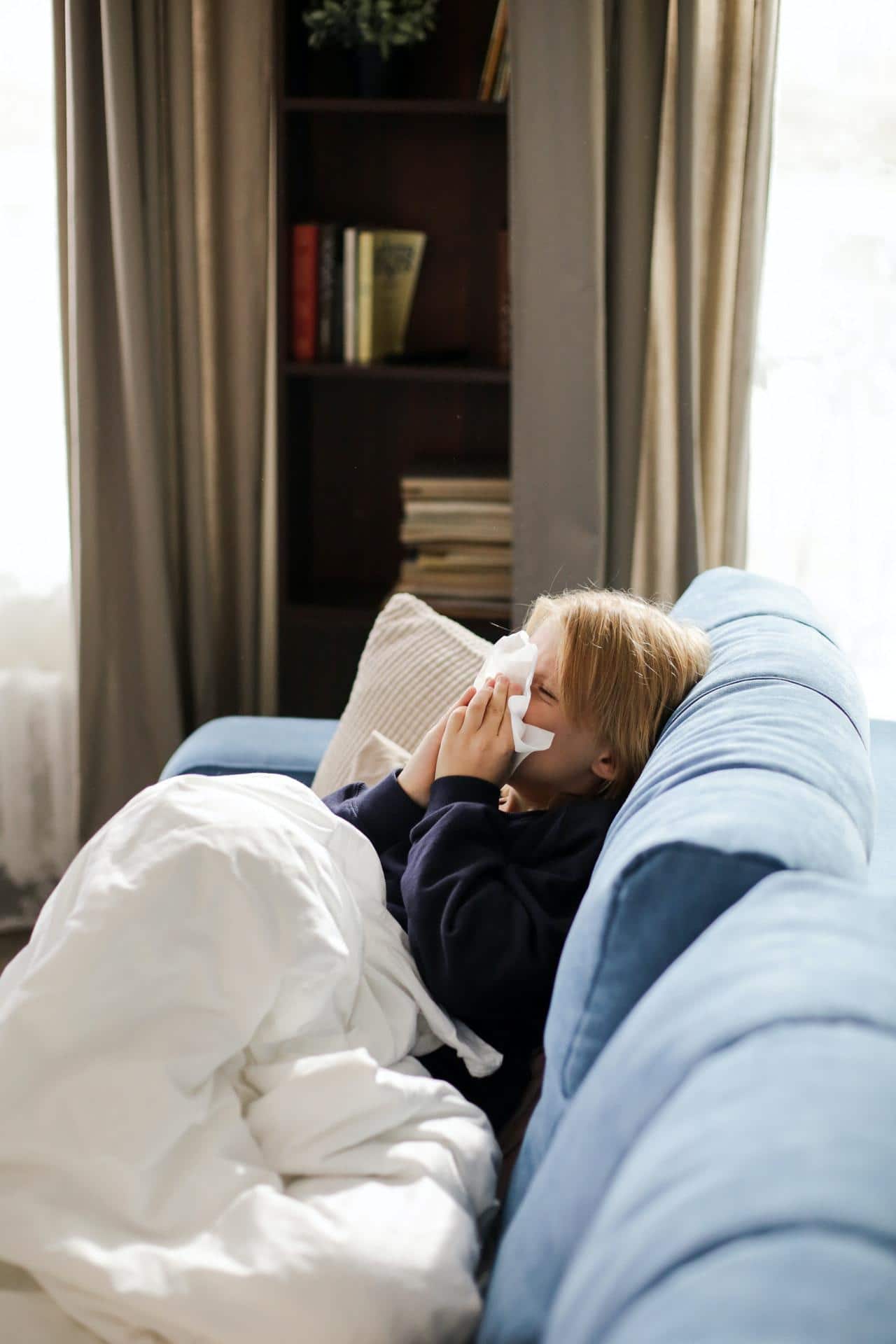 covid or cold child blowing nose on couch