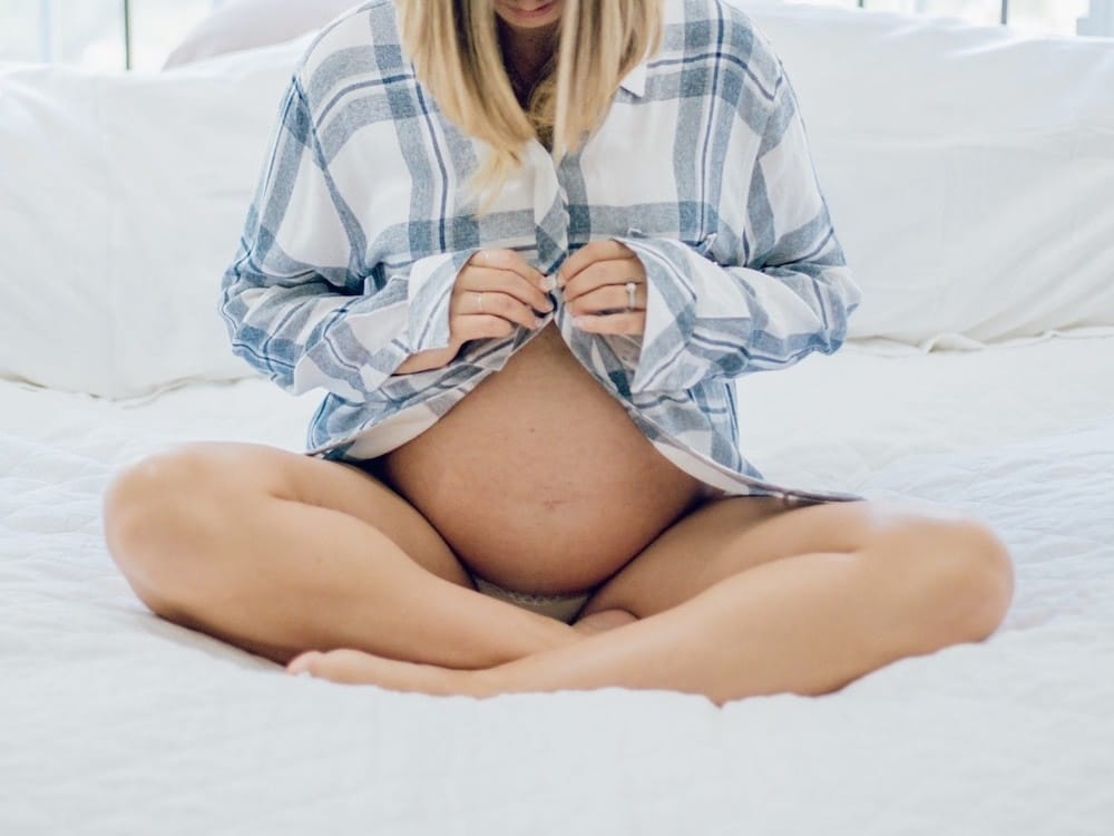 woman buttoning up shirt over pregnant belly