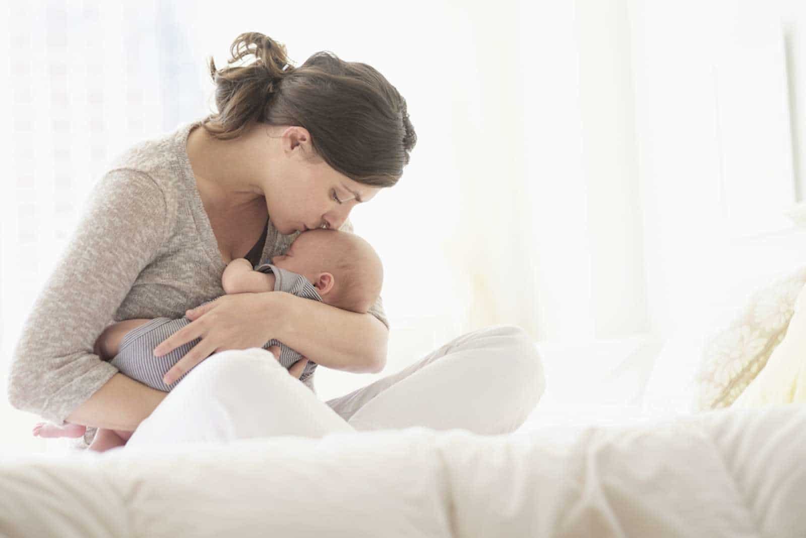 mom kissing newborn on the forehead, thinking about the benefits of singing to your baby