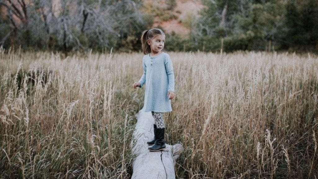 little girl standing on a log outside