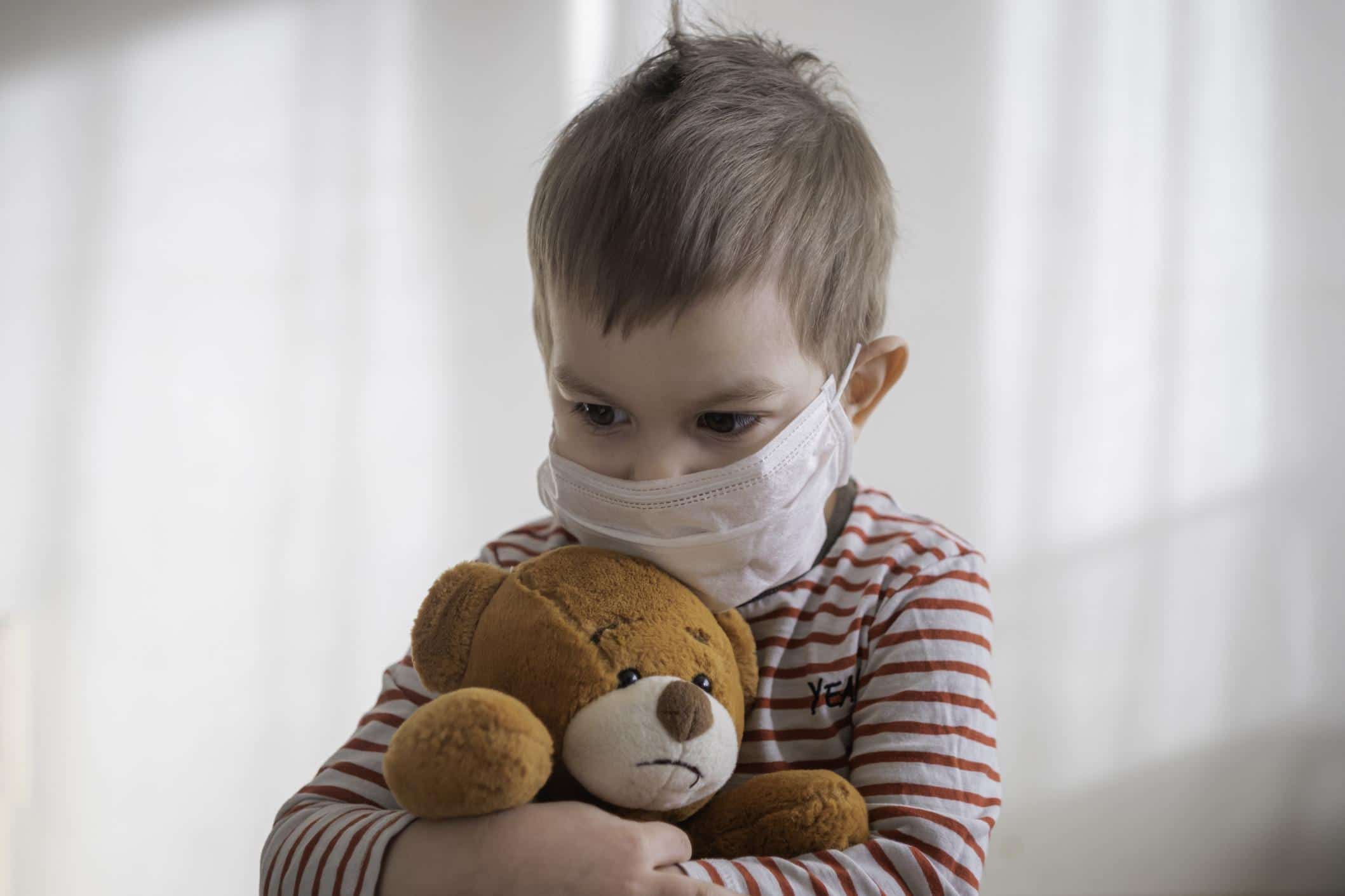 toddler wearing a mask hugging a stuffed bear