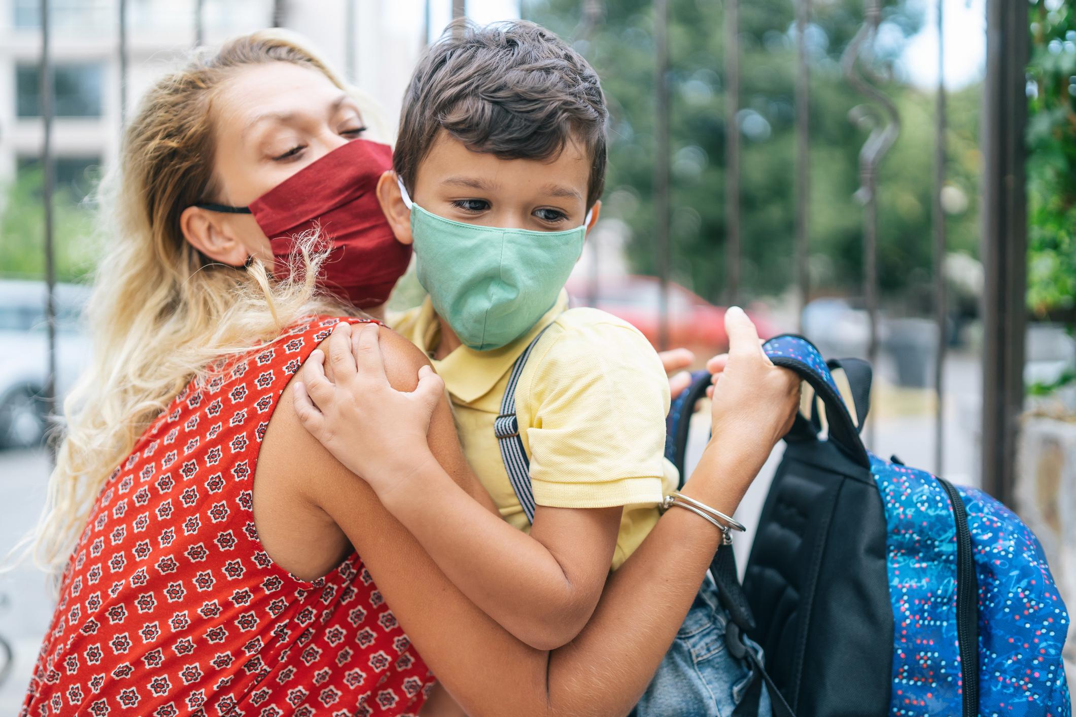 mom hugging child wearing a mask outside of school