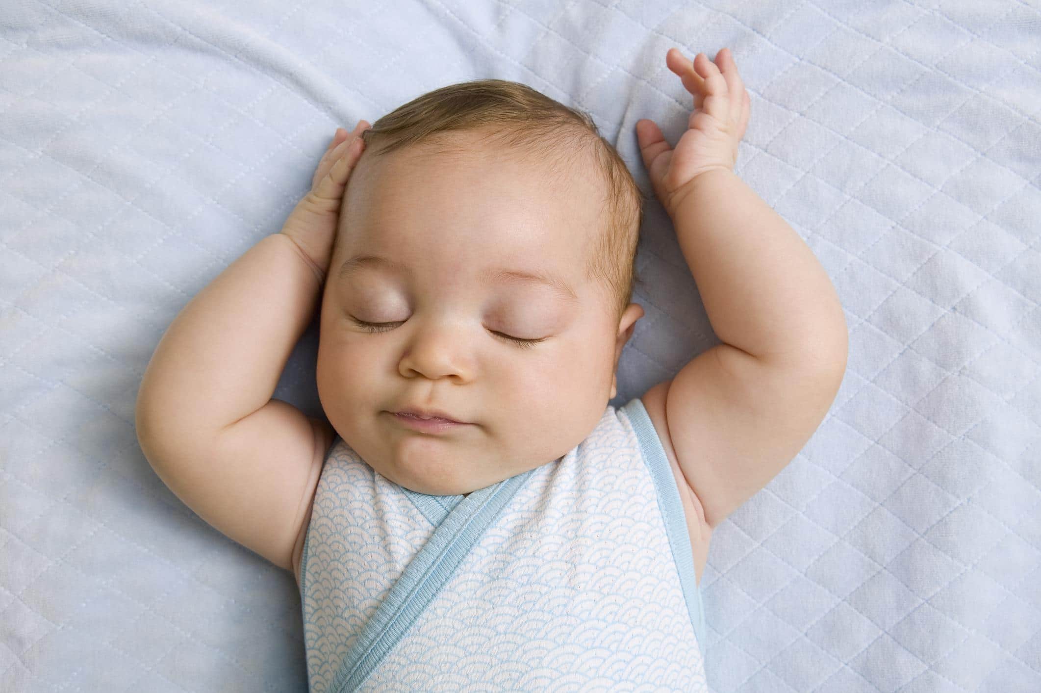 six-month-old baby sleeping with arms above its head